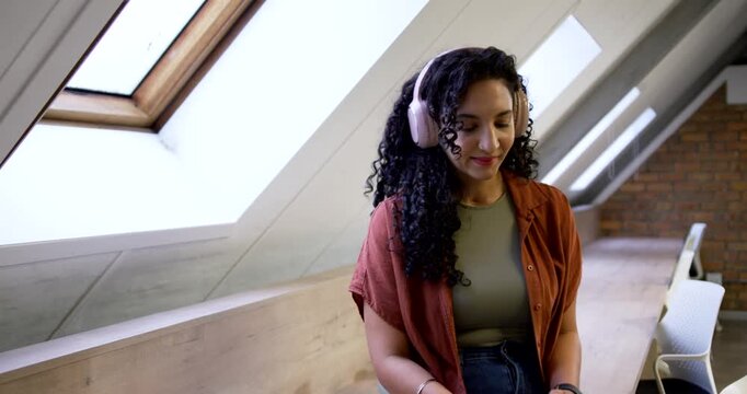 Woman sitting on bench in shirt, pink headphones, noticing skylight and turning, observing outside