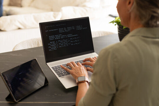 Woman coding on laptop in home workspace wearing olive shirt tablet smartwatch plant, copy space