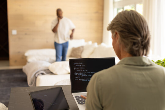 Couple sharing living room, woman coding on laptop at table, man talking on smartphone, copy space
