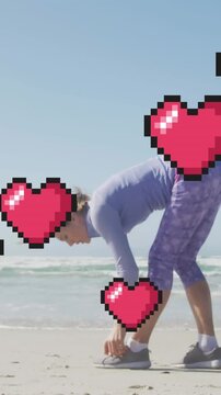 Animation of floating red pixel hearts, over woman tying shoe on beach