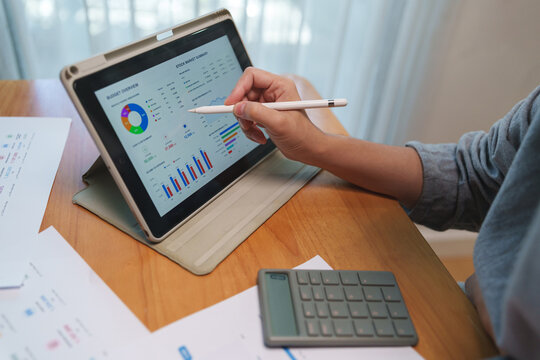 Business professional reviewing a financial dashboard on a tablet with stylus, analyzing market data, charts, and reports for planning and performance evaluation.