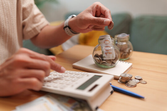 Man saving coins into a glass jar while using a calculator, illustrating budgeting, expense tracking, emergency savings, and disciplined financial planning for future goals.