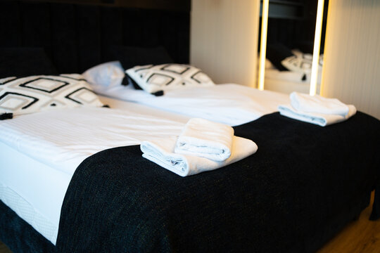 Cozy twin beds with white and black geometric pillows and blankets in a luxury apartment. Neatly folded white clean towels for guests on top of the mattress. Concept of hospitality, tourism