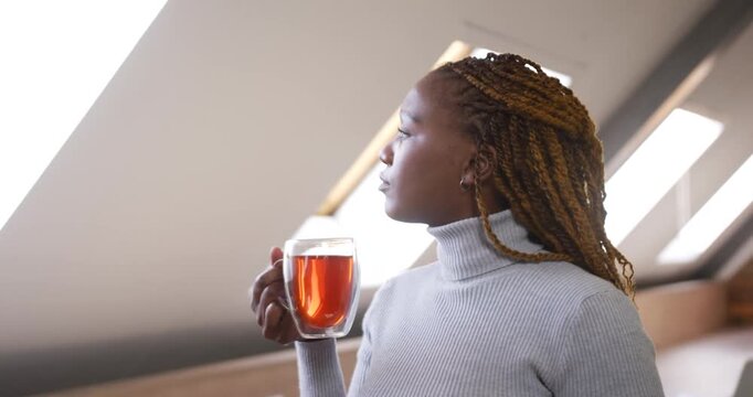 Mid-adult African woman holding phone and mug seeing skylight glancing, musing, sipping, copy space