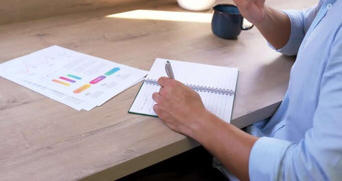 Man reviewing charts, tapping pen on notebook, lifting phone and sending update at desk, copy space