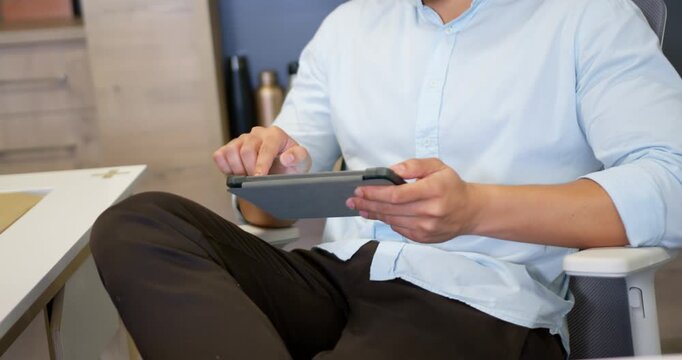 Asian man starting by tapping tablet, holding case and swiping to review work at desk
