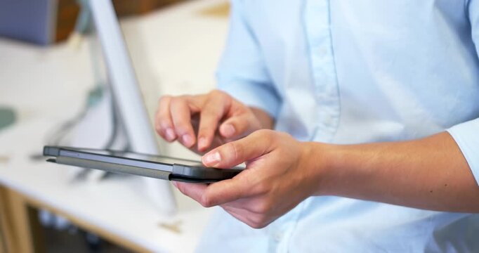 Man in blue shirt holding tablet case tapping top-left while swiping screen at desk, browsing app