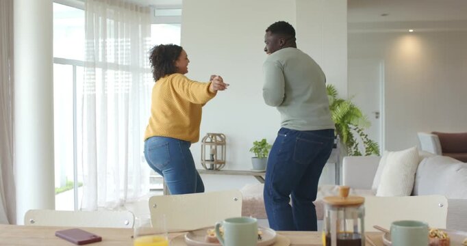 African American couple mimicking phone call, dancing playfully in home, dining table with phone