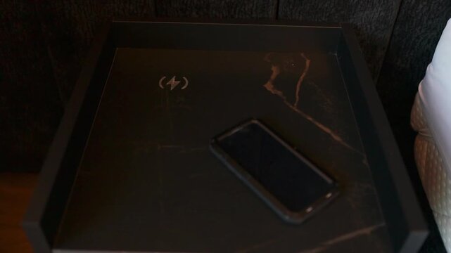 Close-up of a mobile phone screen up on a black luxury nightstand in bedroom. Concept of wireless technology, digital connectivity, morning screen time checking, and minimalist interior design.