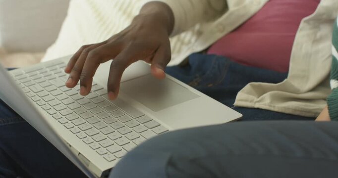African American couple on couch, man typing on silver laptop as woman leaning, reacting to screen