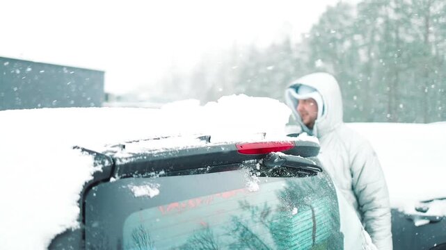 Close-up of a person clearing fresh white snow off an automobile front window and wipers after blizzard. Winter vehicle maintenance, automotive care, and freezing weather concept.