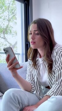 Sad young woman sitting on a sofa at home crying after reading a bad message on her phone, feeling heartbroken and lonely with tears in her eyes after a breakup