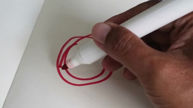 A close up view of a hand drawing a red circle on a white paper surface.