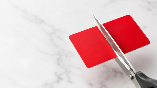 Scissors cutting a red plastic credit card in half on a marble surface