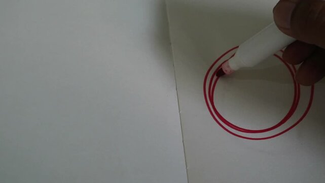 A hand drawing a red circle on a white piece of paper.