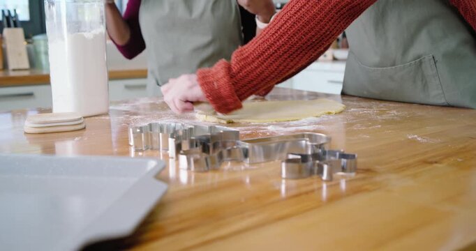 Diverse female friends sprinkling flour then rolling dough, making cookies in kitchen with cutters