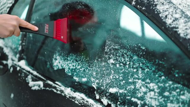 Close-up of a person hands brushing fresh deep snow off an iced automobile window outdoors in winter. Vehicle maintenance, routine care, and cold freezing weather concept.