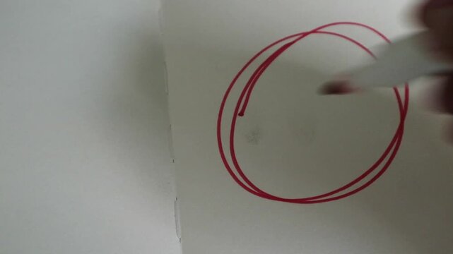 A hand drawing a red circle marker on a white piece of paper with a marker.