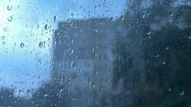 Cool blue rain falling heavily on glass with blurred modern city building outside, isolated