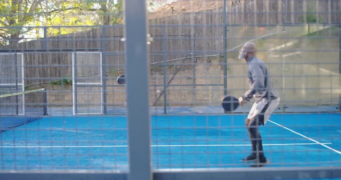 Diverse men rallying on blue-court after man in gray hitting overhead volley with paddle for fun