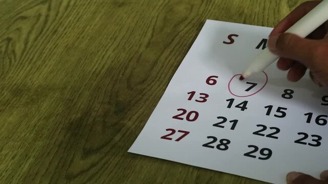 Person circling a date on a paper calendar with a marker pen.