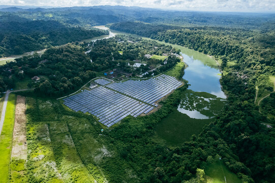 Aerial view of the Kaptai 7.4MW Solar Power Plant situated along the riverbank, surrounded by lush green hills and dense forest in Kaptai, Chittagong Division, Bangladesh.