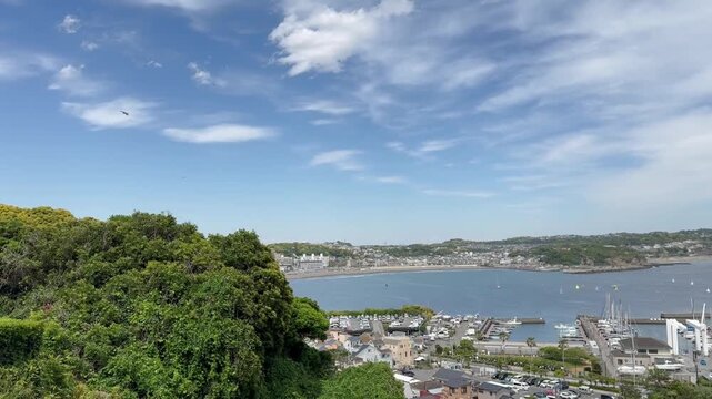 Static high angle shot from Enoshima Island looking toward the mainland harbor and Katasekaigan coastline in Japan with black kite birds circling in a blue sky