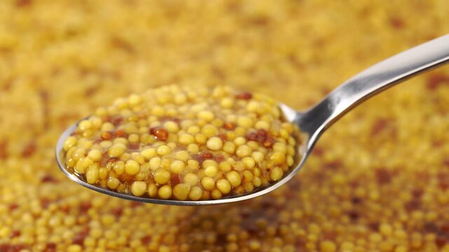 French Dijon mustard in a metal spoon, top view on mustard grains background. Gastronomy concept, organic food. Sauce. Slow rotation in a circle.	
