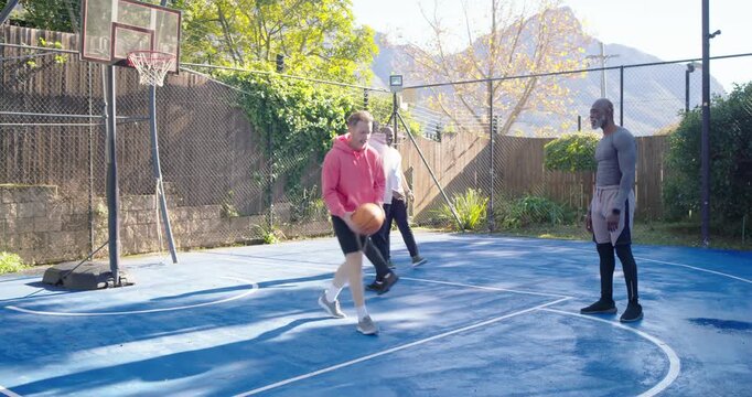 Male friends getting ball leading hoodie player dribbling shooting for score at hoop on blue court