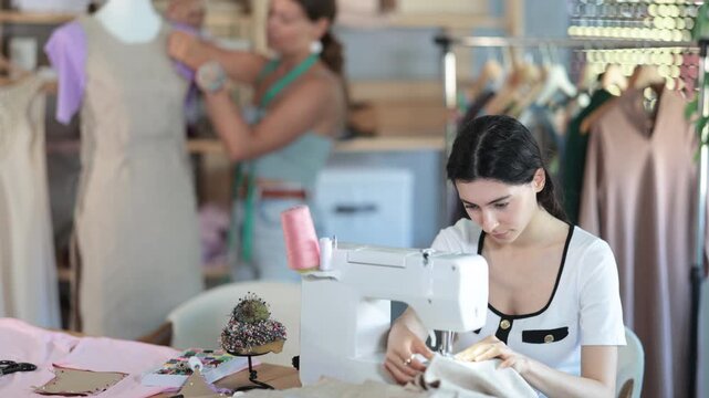 Team of dressmakers works on ordering clothes from a sewing workshop. Fashion designer checks the dress sample on a mannequin, and the seamstress works at the machine. High quality 4k footage