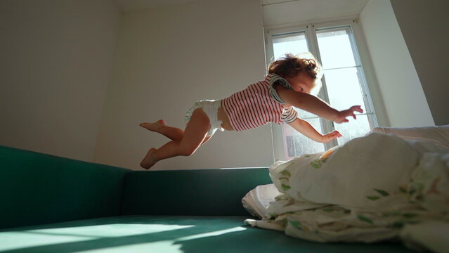 Toddler diving through the air toward blankets on couch at home, carefree action expressing playful freedom, energetic adventure and joyful childhood excitement