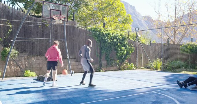 Two men, pink-hoodie and grey defender, fighting for ball to score after shot on backyard court