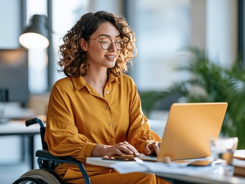Person in wheelchair works on laptop in a bright office space during the day