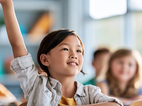 Child raising hand in classroom during school lesson with other students present