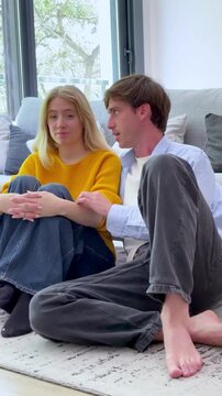 Caring boyfriend comforting his sad girlfriend while sitting on the floor in their living room, having a serious conversation about relationship problems and offering support and understanding