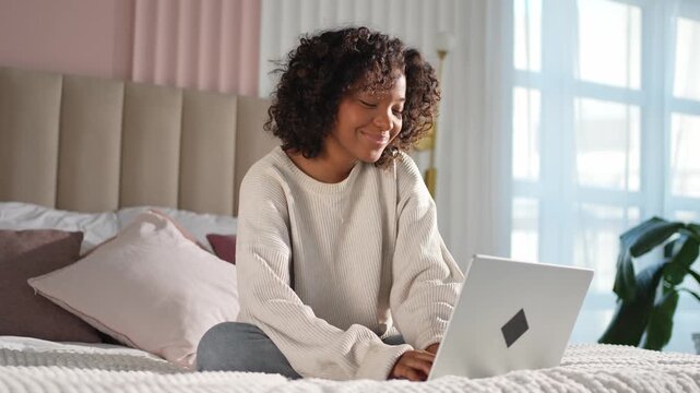 African American girl using laptop in bed at home office typing chatting reading writing email. Young black woman having virtual meeting online chat video call conference. Work learning from home
