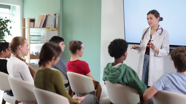 Focused female doctor explaining medical topic to attentive teenage students in modern classroom. High quality 4k footage