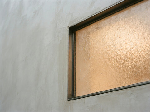 Textured glass window inset within a gray concrete wall and dark metal frame