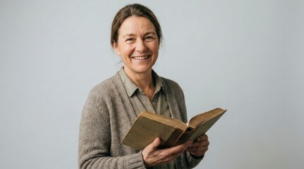 Obraz premium Smiling mature woman holding a vintage book against a neutral background