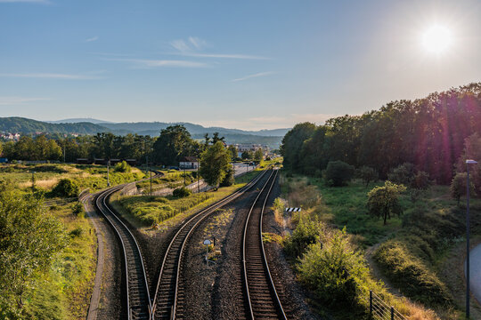 Railway tracks splitting in two directions through rural landscape under bright sunny sky, choice of directions and travel concept