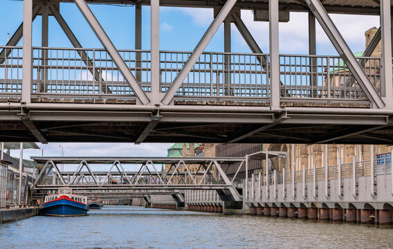 Steel truss pedestrian gangway bridges over canal water with tour boat docked at Landungsbr&uuml;cken in Port of Hamburg, urban architecture concept