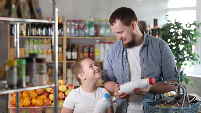 Man with son hold packages bottles and choose consider milk in store. Market visitor choose consider make choice bottle milk. Client hesitates before buying, chooses drink, reads labels on bottles