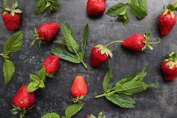 Fresh red strawberries and mint leaves scattered on a dark slate background, featuring a vibrant flat lay composition of organic summer ingredients. © Diana