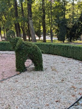 Elephant-shaped topiary sculpture in a formal landscaped garden, surrounded by manicured hedges, mature trees and a gravel pathway.