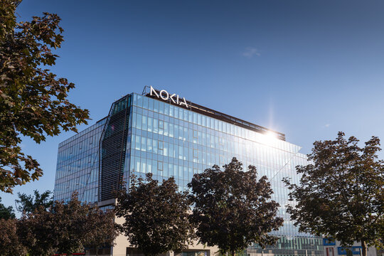 Timisoara, Romania Modern glass facade of the Nokia office building under a clear blue sky with bright sunlight flare, framed by leafy Acer platanoides trees.