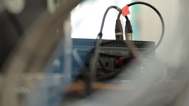 Audio cables with XLR and RCA connectors are plugged into the rear panel of a sound mixer console next to a flight case in a studio setup.