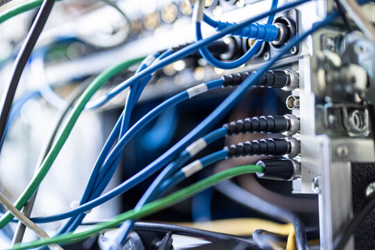 A detailed close-up of blue and green SDI and audio cables connected into the rear patch panel of a broadcast server rack in a professional production unit.