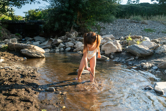 A young white child playing with a stick in a shallow creek outdoors