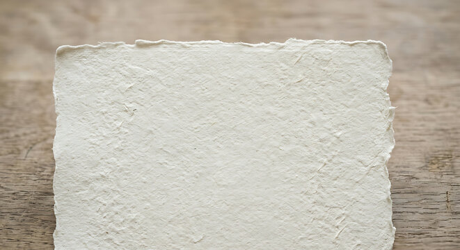 Rustic blank handmade paper with deckle edges and a heavily textured surface lying on a vintage wood table for a minimal aesthetic look