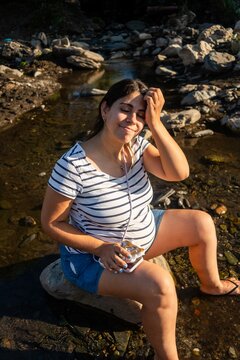 Pregnant woman relaxes by a rocky riverbank enjoying warm sunlight